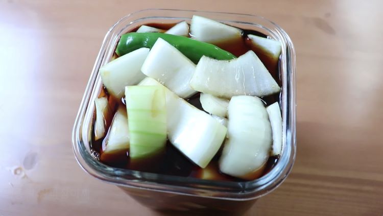 투명한 유리병에 담긴 황금색 양파 장아찌, 아삭하게 썬 양파와 빨간 청양고추가 보이는 모습, 깔끔한 주방 배경에서 자연광으로 촬영한 음식 사진