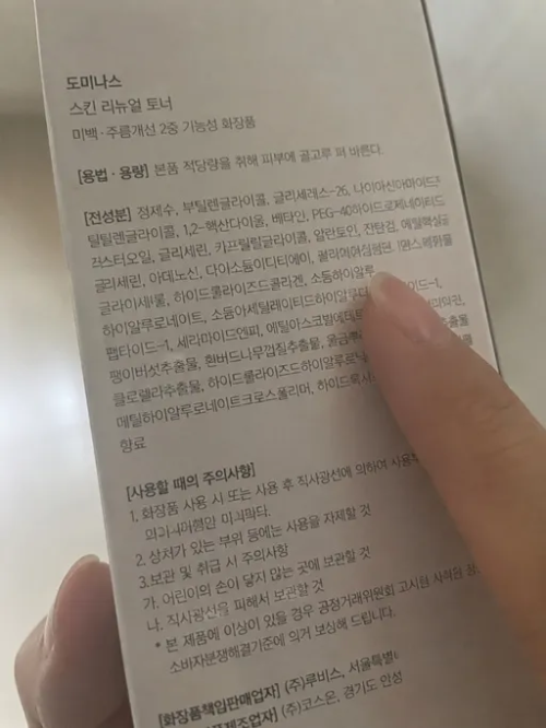 미백 주름개선 기능성 화장품 단상자 뒷면의 전성분과 주의사항을 손가락으로 짚어가며 꼼꼼하게 확인하고 분석하는 모습