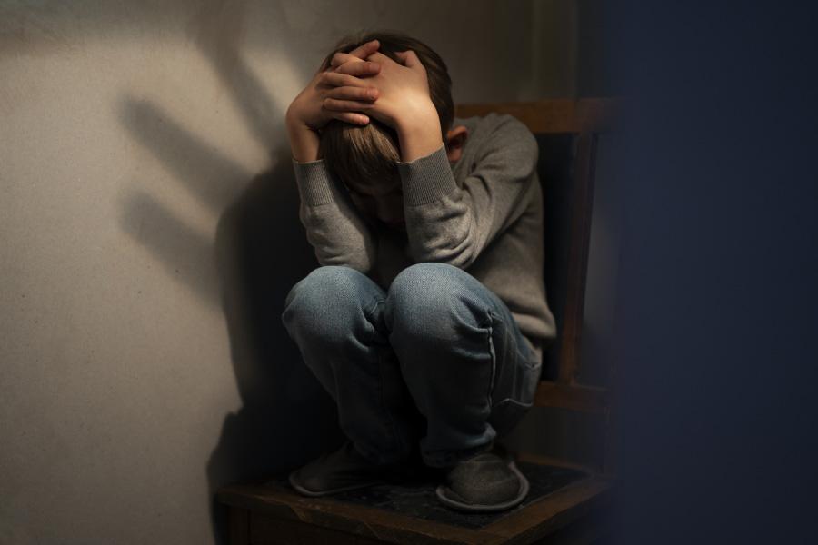 한 어린 학생이 광장공포증으로 인해서 두려움에 어두운 방구석의 의자에 청바지와 긴팔을 입고 쪼그리고 앉아서 머리를 손으로 감싸며 고통스러워 하고 있는 사진