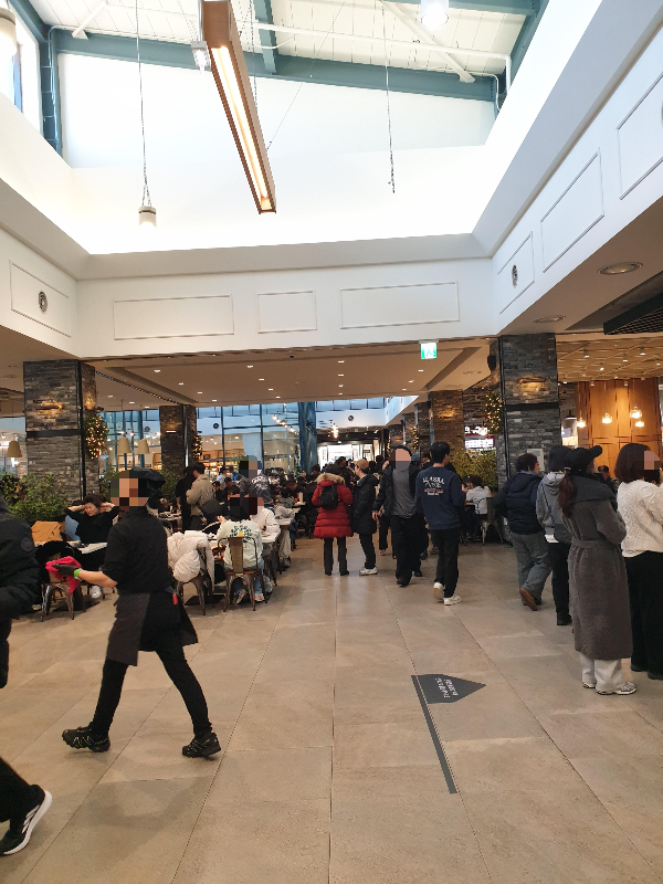 현대 김포 아울렛 푸드코드 중간 통로 넘어 자리잡은 사람들과 서 있는 사람들이 보인다.