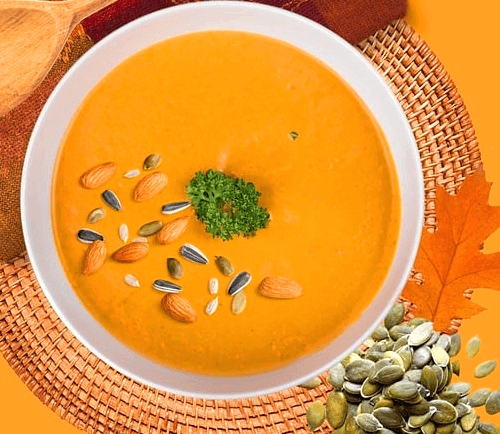 하얀 그릇에 노란 호박죽이 가득하다. 주변엔 녹색의 호박시가 있다.