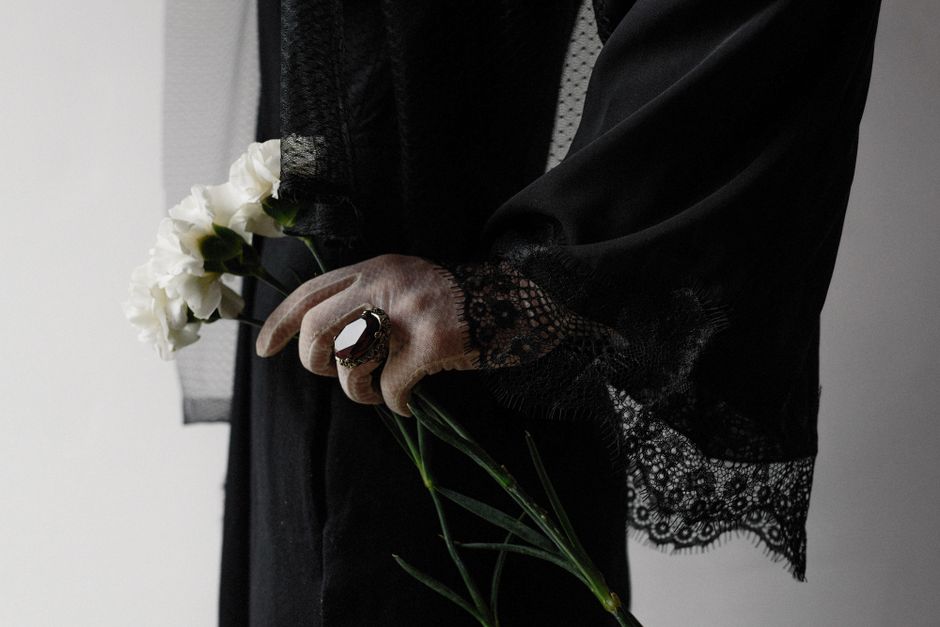 Close-up of a woman in black lace dress holding white flowers, symbolizing mourning and elegance.