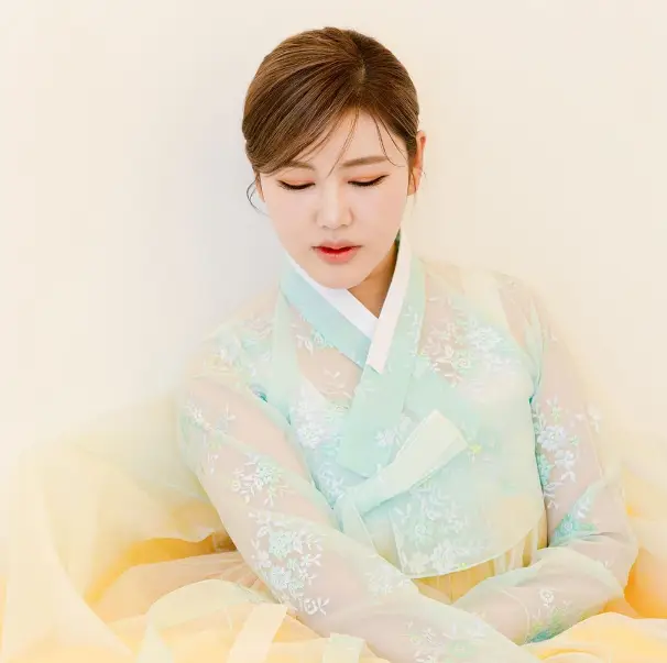 송가인-
베이지색 배경 앞 노란 치마 하늘색 저고리를 입고 쪽진머리로 땅을 바라보는 송가인