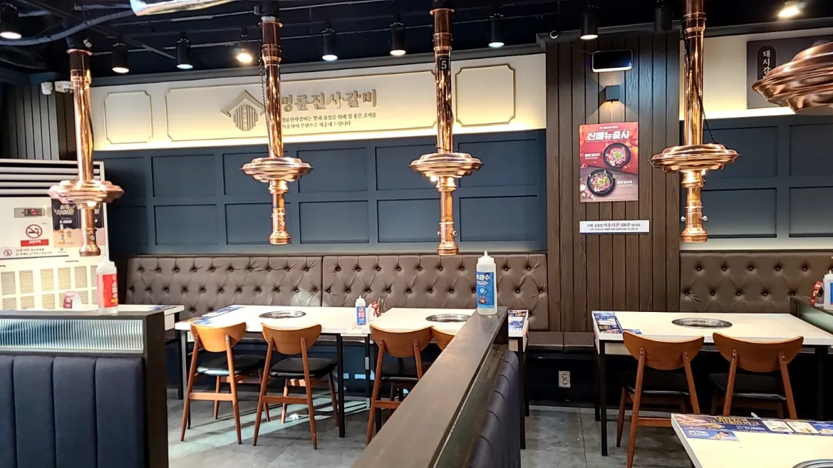 명륜진사갈비-실내-흰색테이블이-3개옆으로길게-놓아져있고-위에는-반짝거리는연기흡입기가-연결되어있다