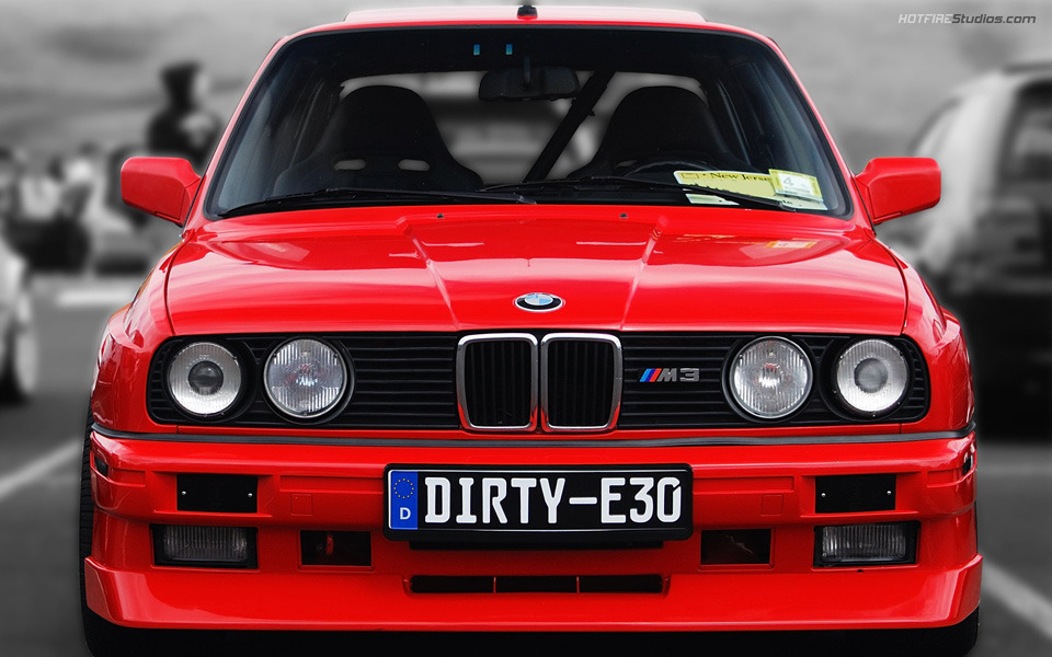 A classic red BMW 3 Series E30 parked on a scenic road, highlighting its iconic kidney grille.