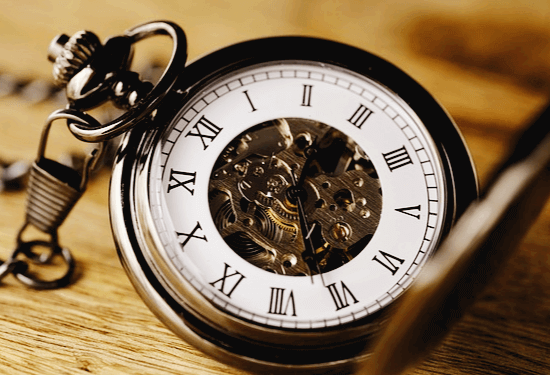 동그란 줄시계가 나무 탁자 위에 있다. 시계 표면은 고동색이고 알림판은 하얀색이다.