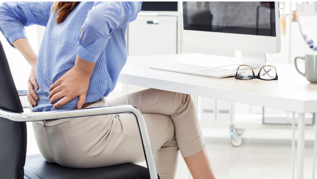 사무실에서 허리를 부여잡고 앉아 있는 여성. 장시간 앉은 자세로 인한 허리 통증을 표현한 장면.