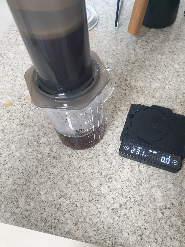 테이블위에 저울과 서버가 있다. 서버 위에는 에어로프레스가 올려져있다. 서버에 커피가 일부 추출된 모습