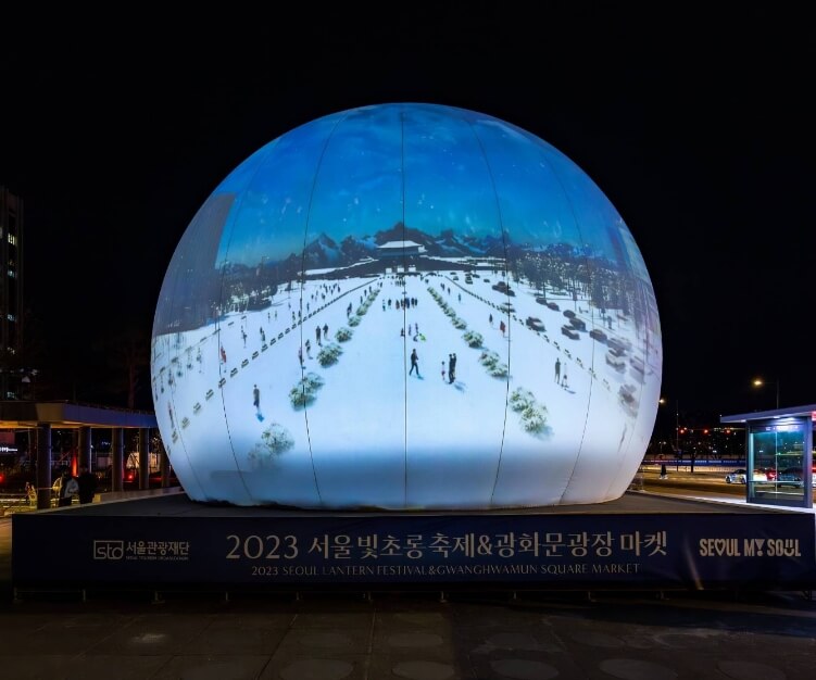 대형 구형 조형물에 겨울 풍경과 사람들이 투영된 화면이 나타나며, 광화문광장 마켓을 알리는 텍스트가 하단에 위치한 독특한 조명 설치물