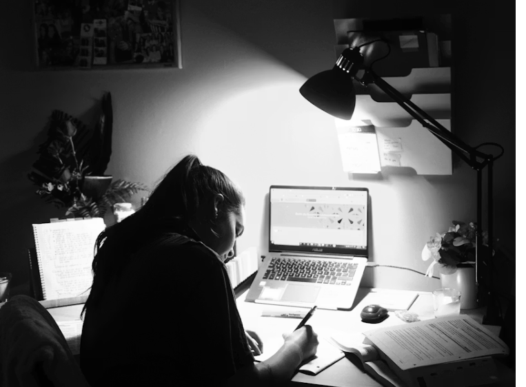 조명이 켜진 책상에서 손으로 글을 쓰고 있는 여성의 모습, 감정 정리나 하루 회고를 하는 장면처럼 보임