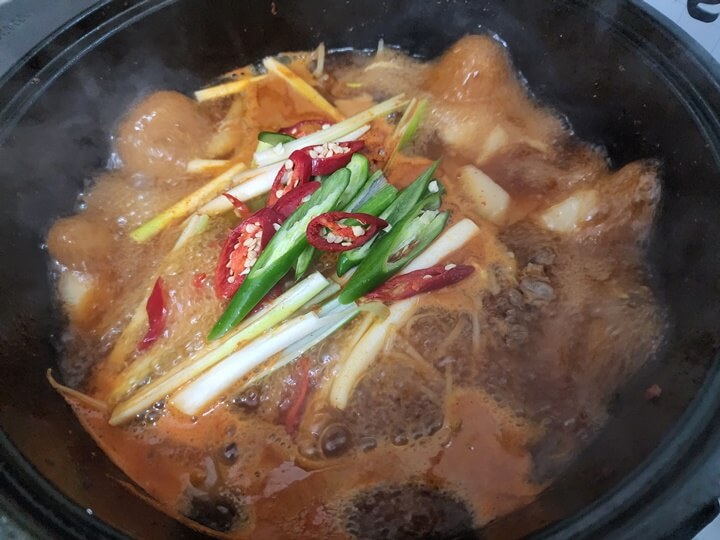 끓고 있는 냄비 안의 쇠고기와 무 위에 올려진 대파와 붉은 고추와 파란색 고추
