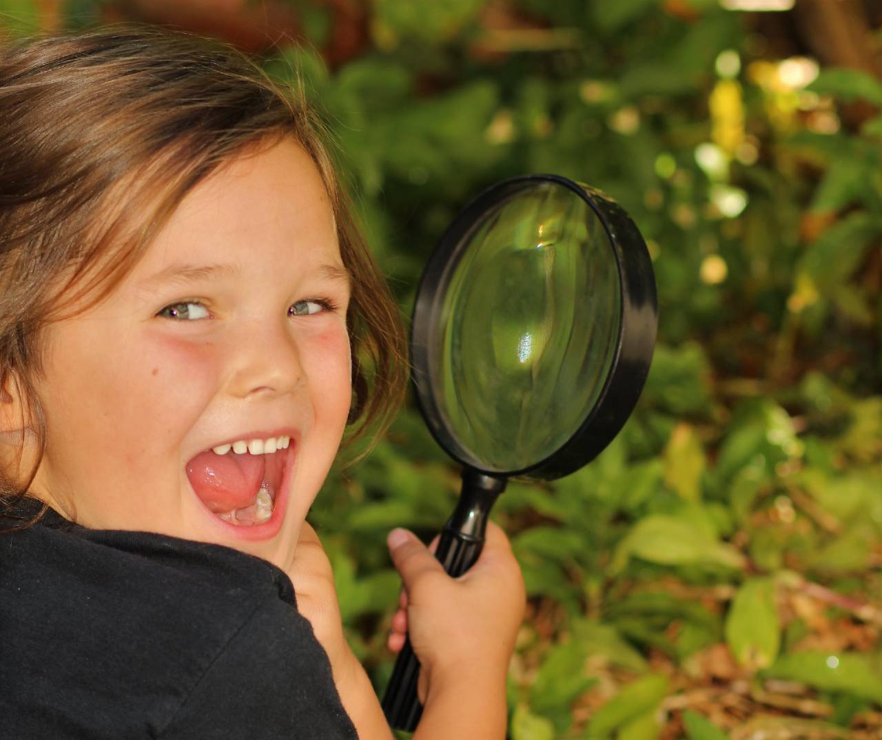 검은색 티셔츠를 입은 어린아이가 돋보기를 들고 웃고 있다