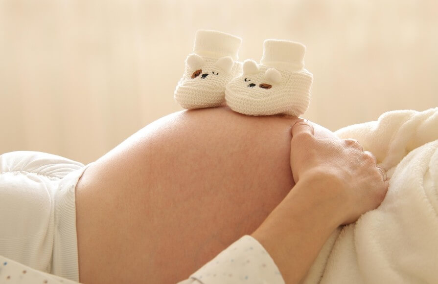임신한 여성이 누워서 아기 신발을 배 위에 올려 놓은 모습