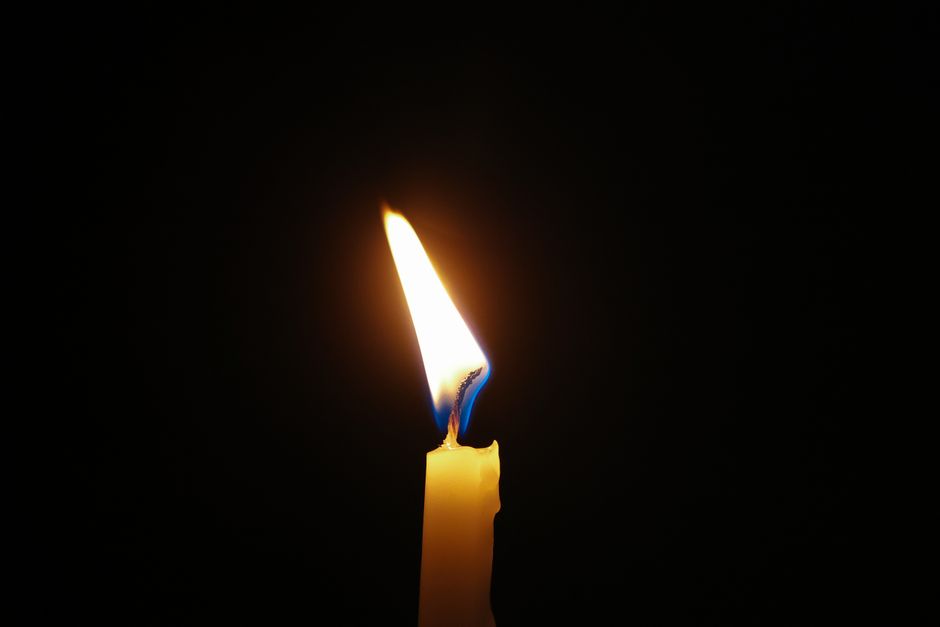 A solitary candle flame glows warmly against a dark background, creating a peaceful ambiance.