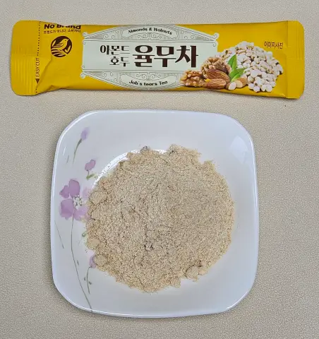 접시에 담긴 노브랜드 아몬드 호두 율무차 분말과 개별 스틱 포장 모습