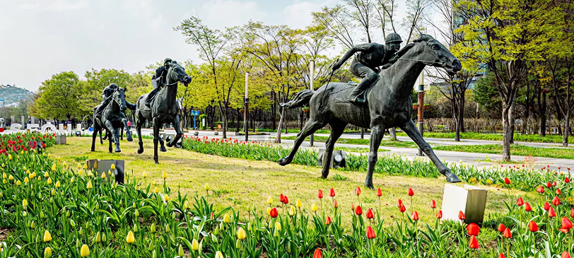 화사한 봄꽃 튤립이 피어난 화단과 역동적인 경주마 조각상이 어우러진 서울숲 군마상 풍경