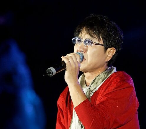 조용필이-빨간-가디건을-입고-색이-들어간-안경을-쓴-채-노래를-부르고-있는-모습