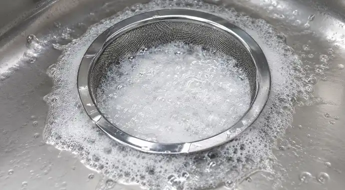 배수구 안에서 과탄산소다와 뜨거운 물이 반응하여 하얀 산소 거품이 피어오르는 디테일