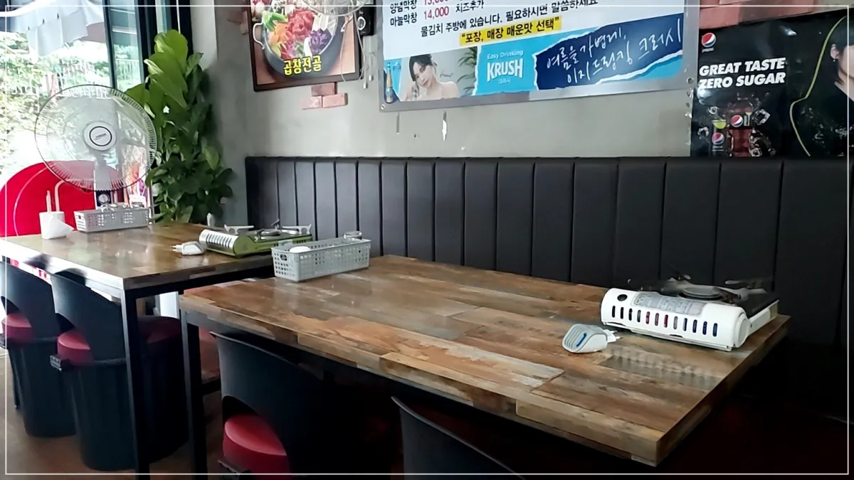 유정곱창식당내부 나무테이블 2개 긴검정쇼파 벽면에는 메뉴판, 테이블 위에는 가스버너