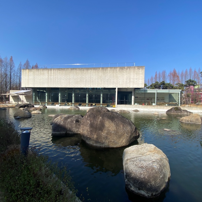 호수에 돌이 있고 노출 콘크리트 건물이 뒤에 있습니다.