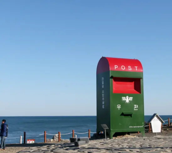 바닷가 옆 초록색 위 빨강색이 어우러진 우체통