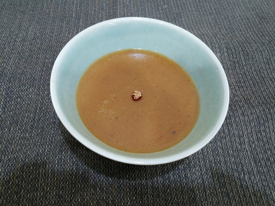 곶감을 넣고 만든 곶감죽을 희고 동그란 그릇에 반쯤 담아두고 회색 바닥 위에 놓아두고 찍은 사진