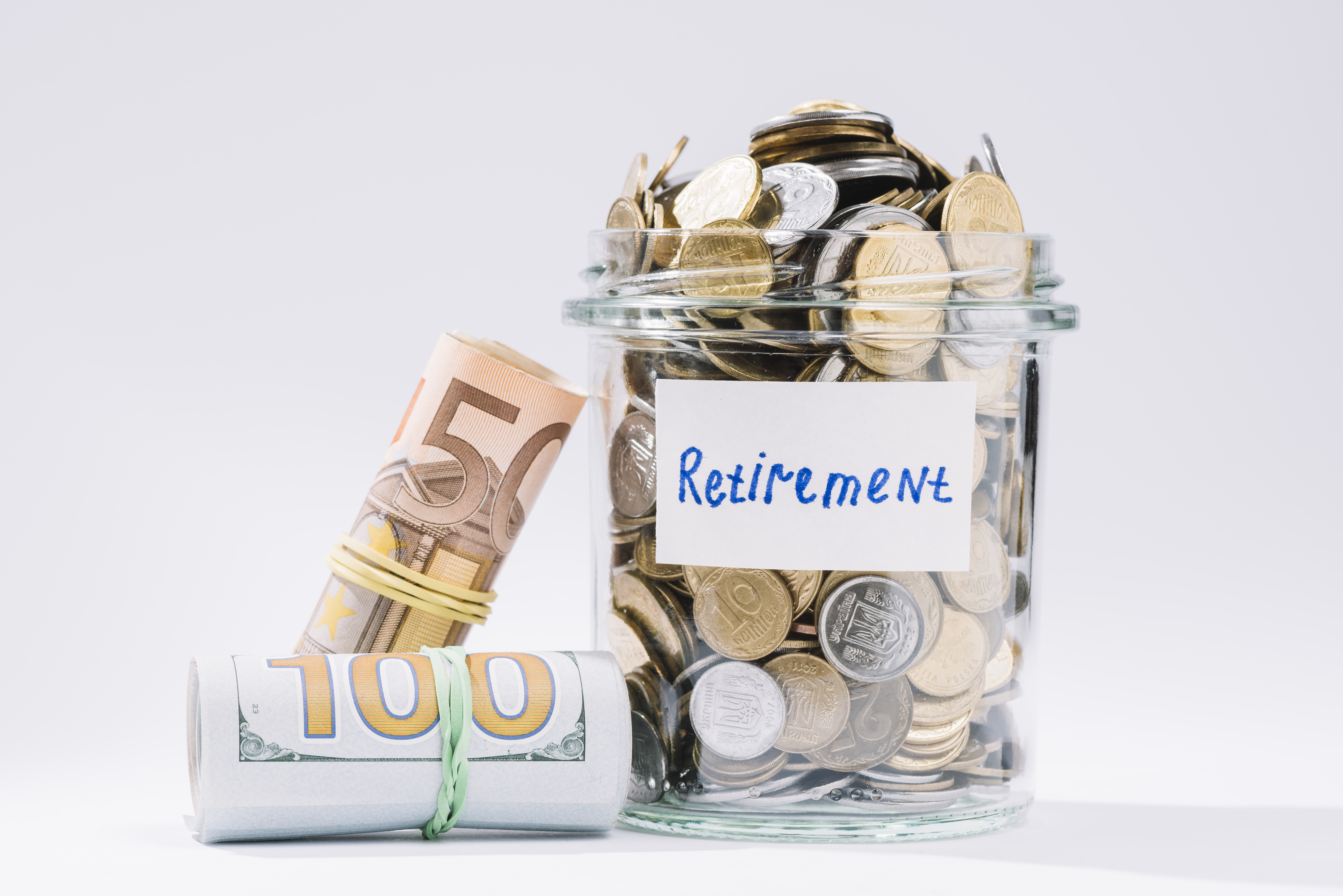 'Retirement'라고 쓰인 종이가 붙은, 동전이 가득 찬 유리병과 그 옆에 고무줄로 묶인 50유로 지폐, 100달러 지폐 두 롤