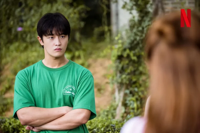 어느 실외를 배경으로 녹색 반팔티를 입고 팔짱을 끼고 있는 드라마 이두나의 구정훈 캐릭터