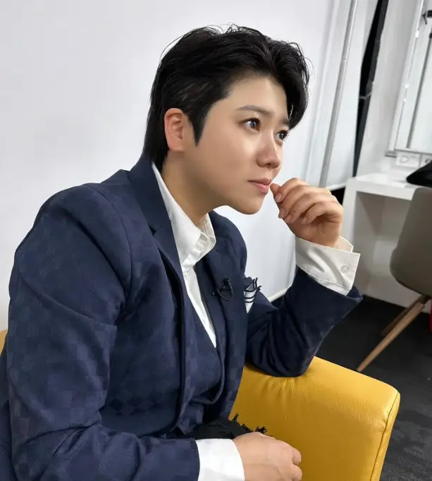 한일가왕전-파란쟈켓을 입고 노란소파에 앉아잇는 마이진