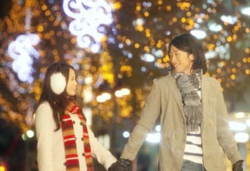 연인이 손을 잡고 서로를 바다보고 있다. 뒤로는 조명이 비치고 있다