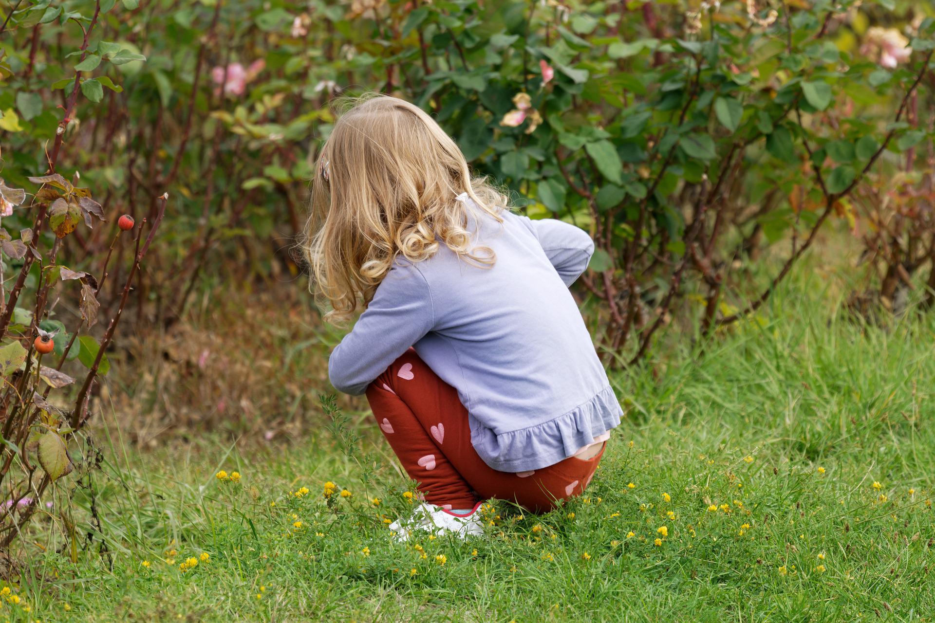 야외에서 쪼그려 앉아있는 금발 여자아이