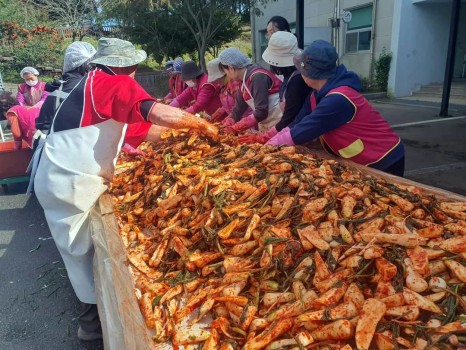 큰 테이블에서 붉은 양념으로 알타리무를 버무리는 사람들