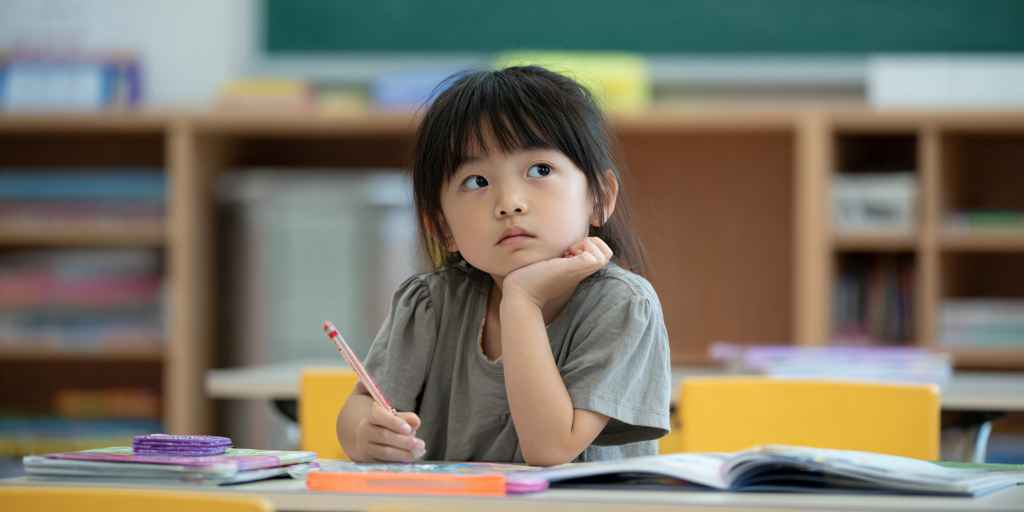 A child is sitting at a desk with an open English book, but looking out the window with a bored expression.