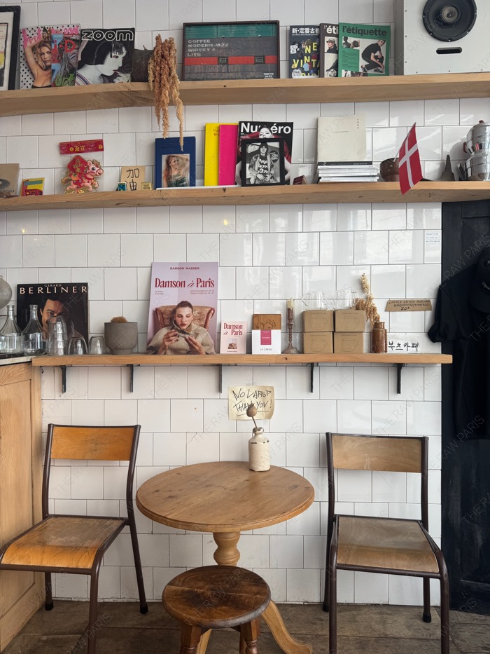 The interior of Boot Cafe Paris with wooden shelves filled with magazines and a small round table ❘ L'intérieur du Boot Café à Paris avec des étagères et une petite table