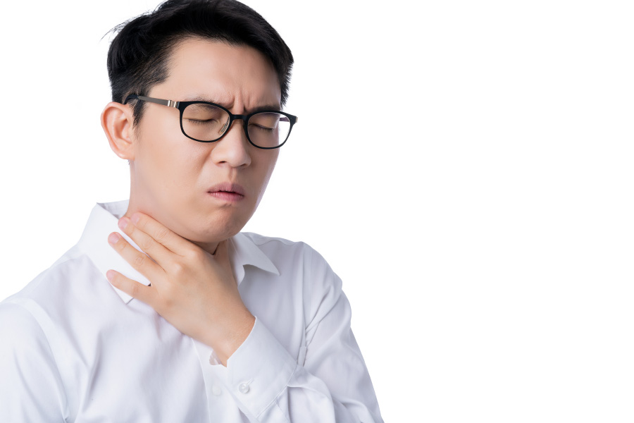 검은색 뿔테 안경을 쓴 동양 남성이 왼쪽 손으로 본인의 목을 감싸고 목이 잠기고 아픈 것을 호소하고 있는 것을 찍은 사진
