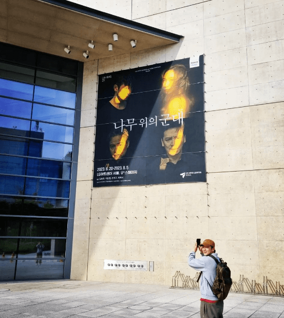 나무위의군대 포스터가 있는 건물 앞에서 사진 찍는 손석구