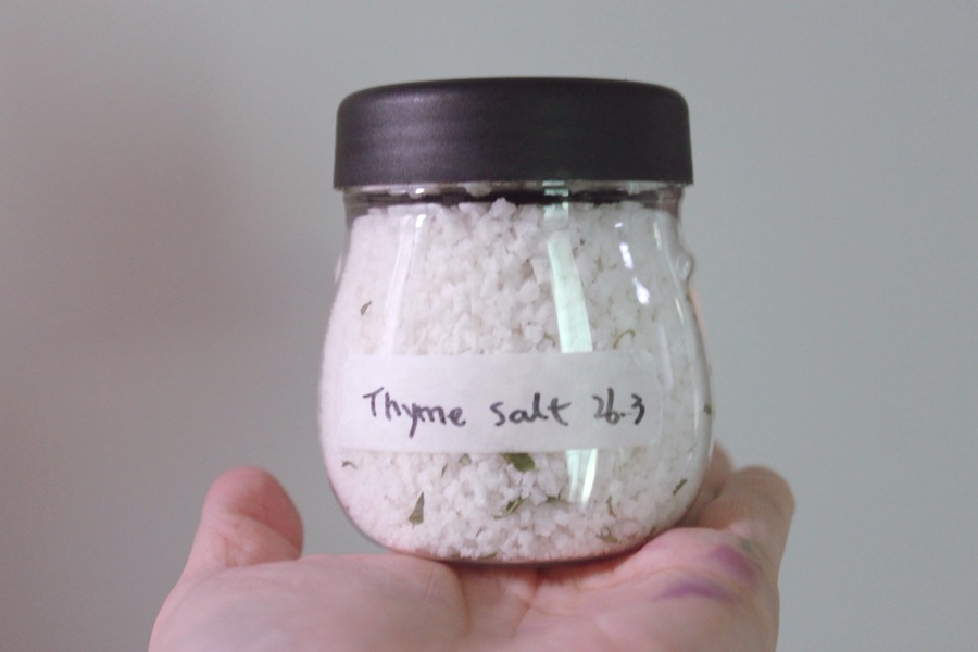 'Thyme salt 26.3'이라고 손글씨 라벨을 붙인 작은 유리병을 손바닥 위에 올린 모습