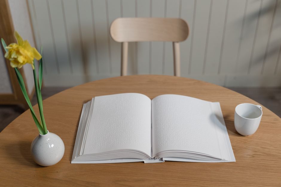 Braille book on wooden table with daffodil flower in vase and cup, indoors