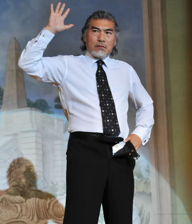 나훈아- 흰셔츠 검은바탕 흰 땡땡이 넥타이를 매고 인터뷰 책상에 올라서 풀어헤친 바지 허리띠를 잡고 서있는 나훈아