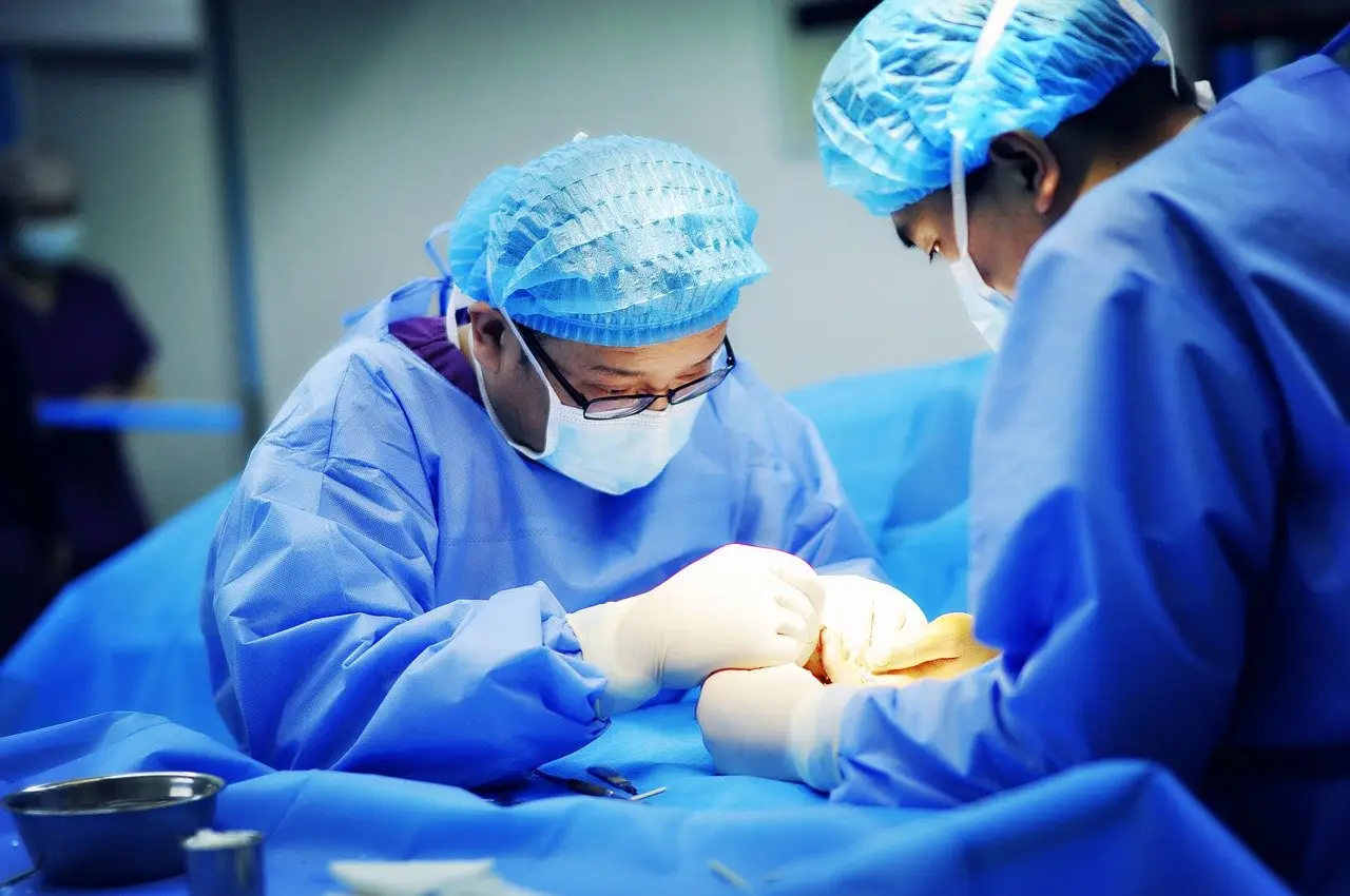 환한 수술실 파란수술복과 파란 모자를 쓴 의사가 집중하여 수술하는 모습
