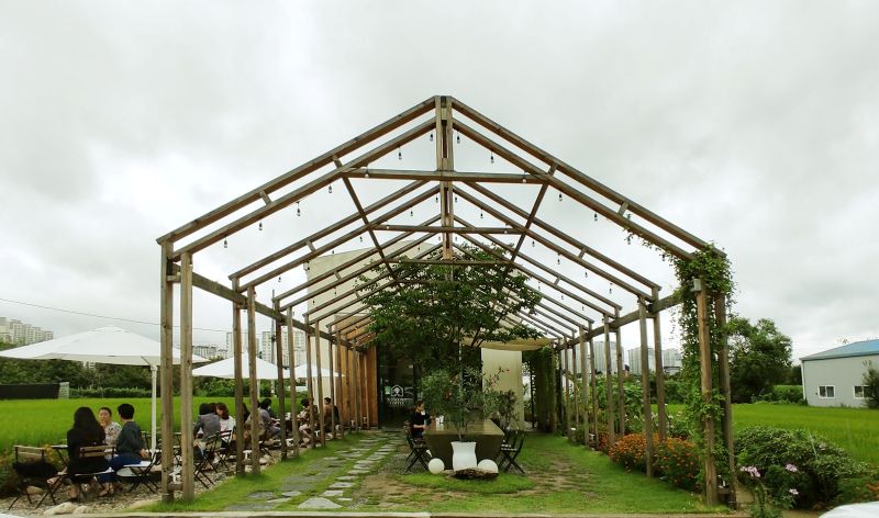 로스터스 야외공간 우유곽모양의 커피숍 앞으로 나무구조물이 있고 야외 조명과 하얀천으로 이색적인 분위기가 드는 아웃테리어