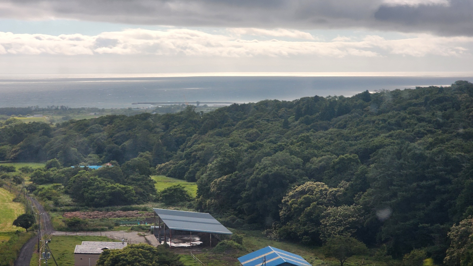 구스타프 말러의 아다지에토 음악과 어울리는 "평화롭고 서정적인 분위기의 제주도 앞바다 전경 사진. 푸른 숲과 마을,멀리 수평선이 보이는 풍경"