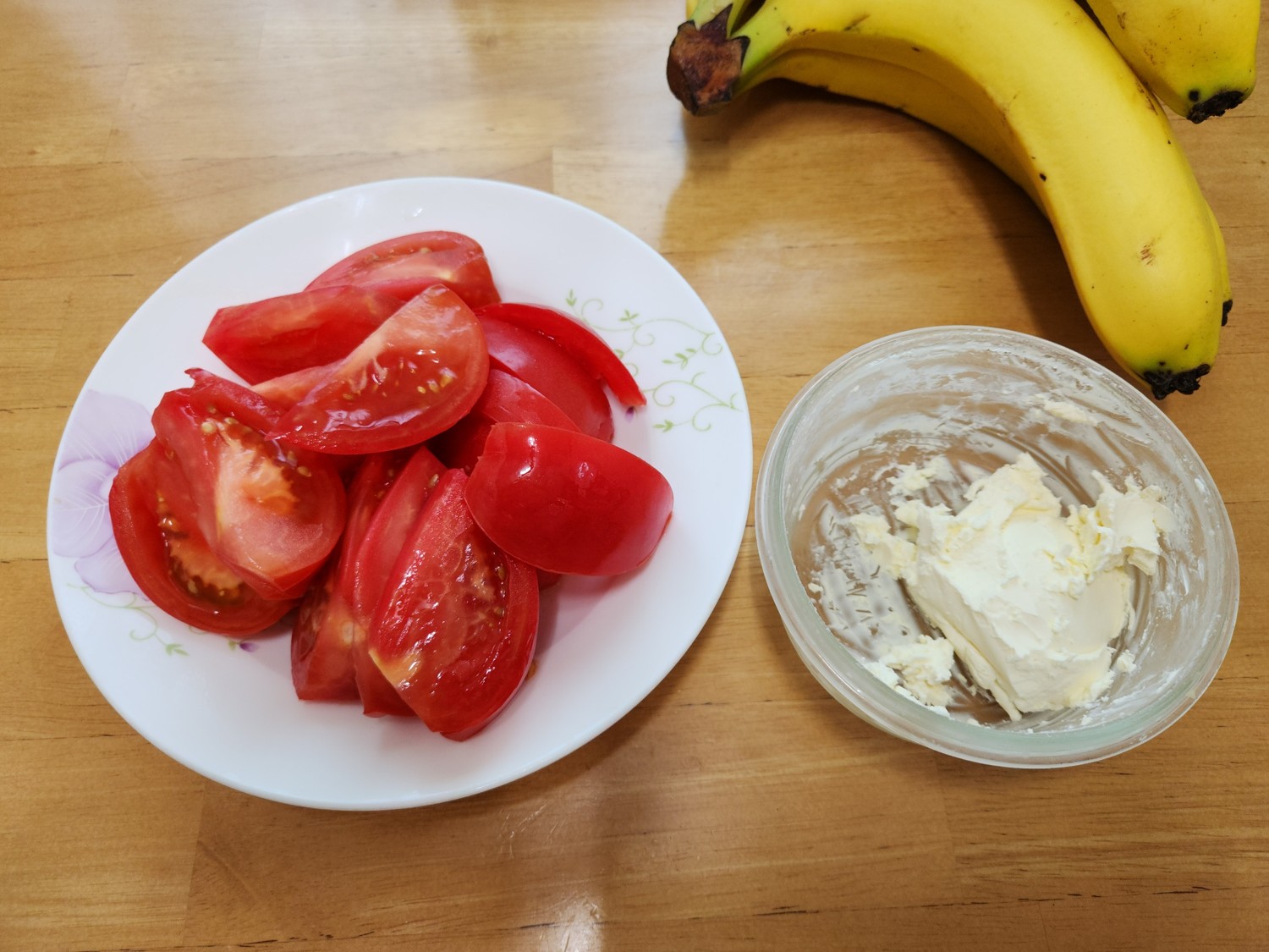 접시에 썬 토마토&amp;#44; 그릇에 크림 치즈가 담겨 있으며 접시와 그릇 사이에 바나나가 있다