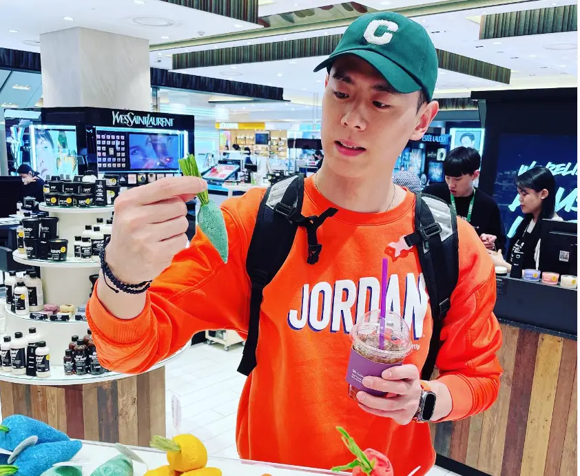 솔로지옥 3 - 주황색 긴팔 티를 입고 초록색 챙이달린 모자를 쓴채 오른손으로 나뭇잎을 들고 나뭇잎을 바라보는 이관희