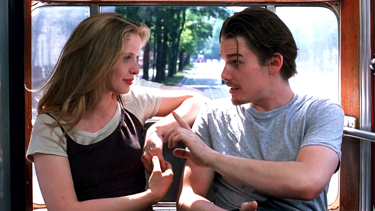 트램 안에서 여자와 남자가 마주 앉아 손짓을 섞어가며 대화하고 있고, 창밖으로 햇살이 비치는 빈의 거리 풍경이 펼쳐져 있다