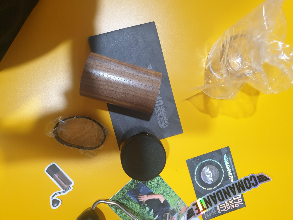 노란 테이블 위에 수동 그라인더 부품과 메뉴얼 그리고 보증서 등이 놓여있다.