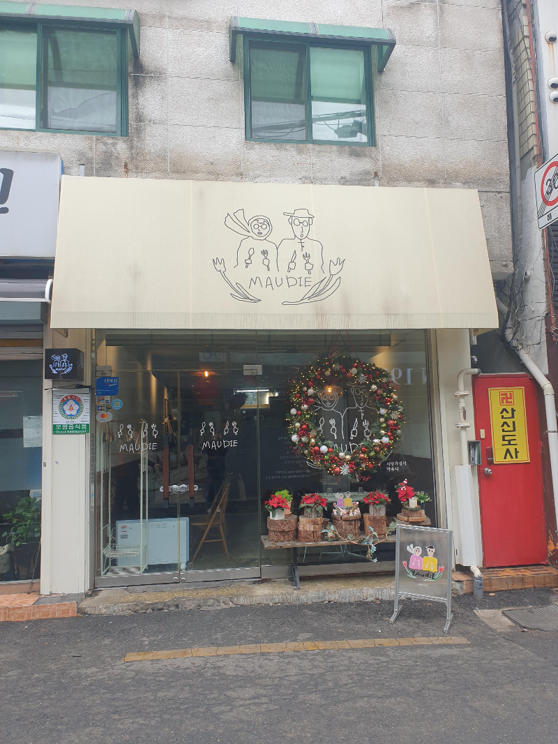 회색 타일로 되어 있는 건물에 베이지색 어닝이 있는 마우디 전면