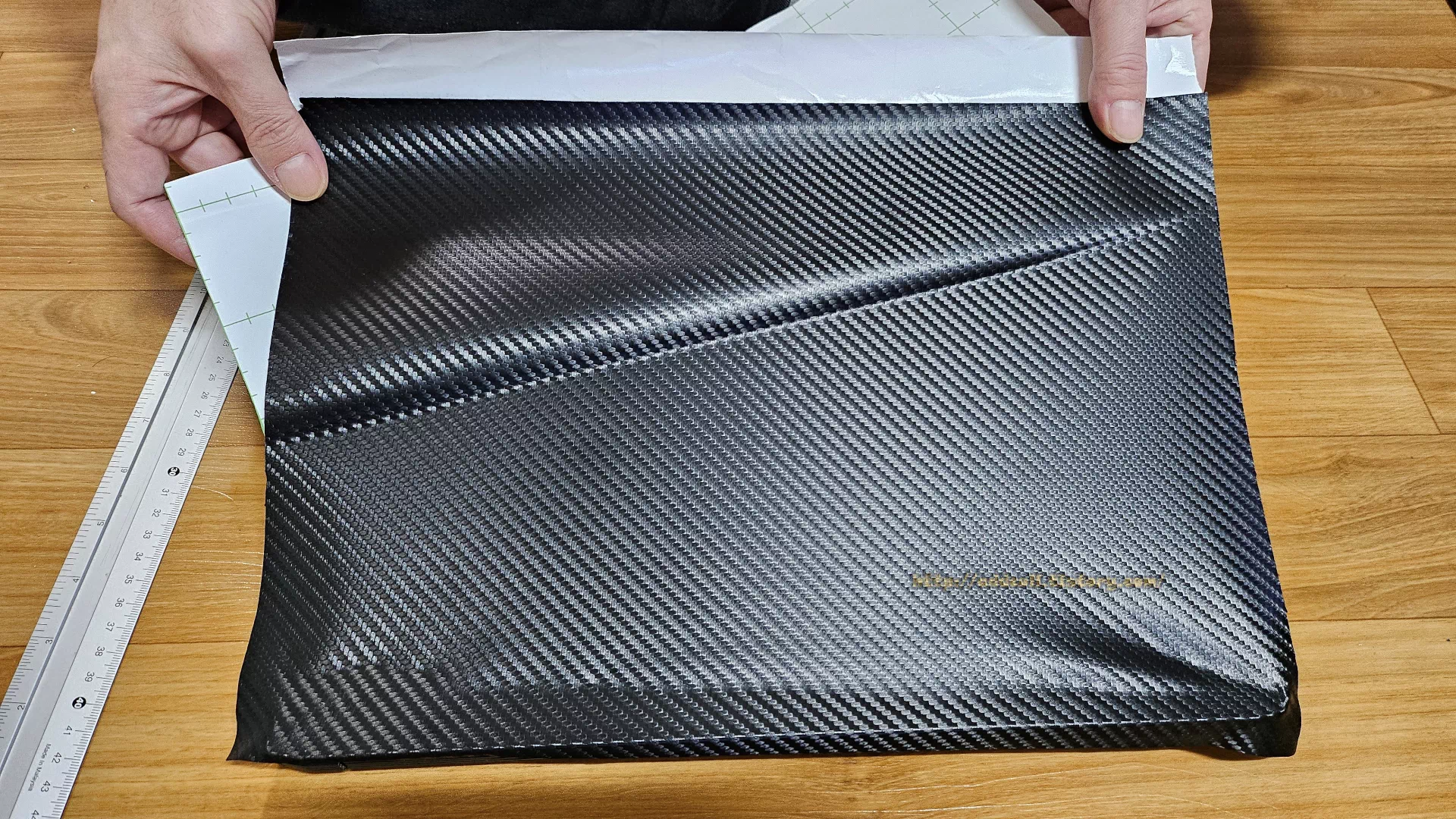 시트지를 노트북 상판에 붙이고 두손으로 조금씩 당겨서 붙이고 있습니다