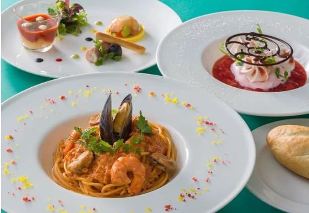 흰색의 동그란 접시 가장자리에 노란색과 빨간색 가루로 장식이 되어 있고 가운데에 붉은빛의 파스타 면이 들어가 있다.