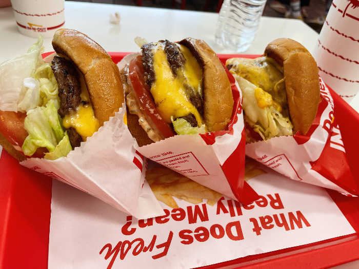 더블 더블 버거 하나와 치즈 버거 두 개가 빨간 쟁반 안에 나란히 세워져 있다.